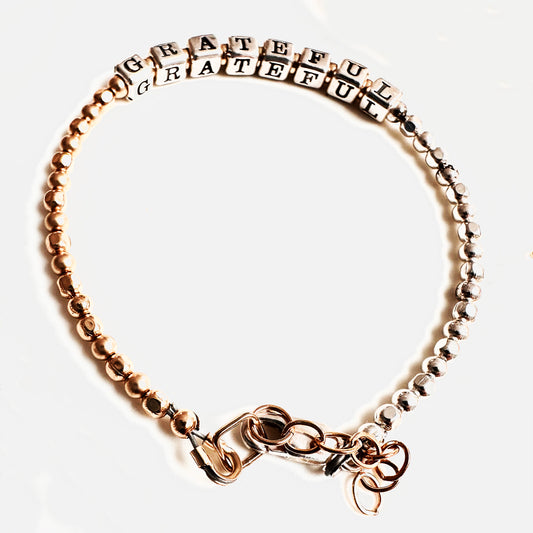 A mixed metal bracelet with alternating sterling silver and 14k gold-filled beads, featuring a clasp and the word 'GRATEFUL' prominently displayed.